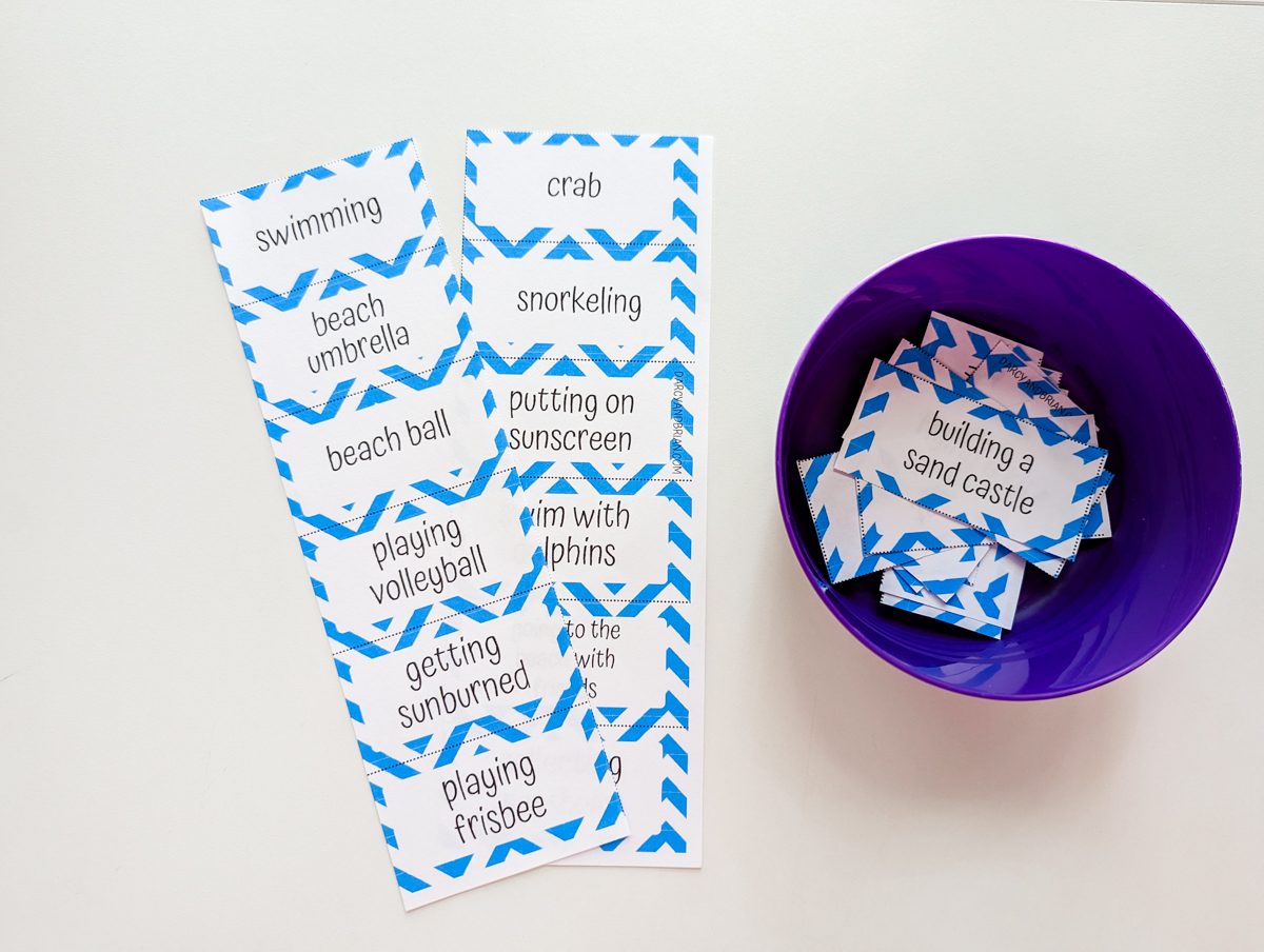 Two strips of charades cards laying next to small purple bowl containing the rest of the cards cut apart.