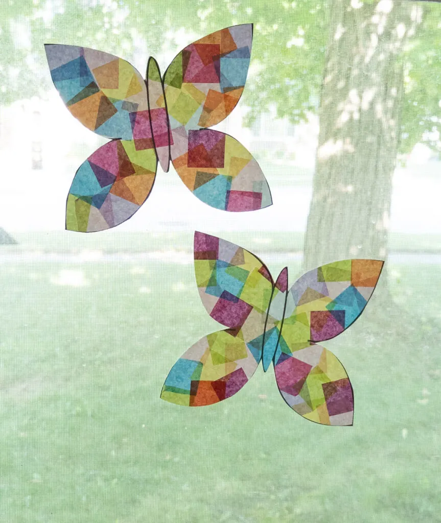 Two colorful paper butterfly suncatchers made without contact paper taped to a sunny window.