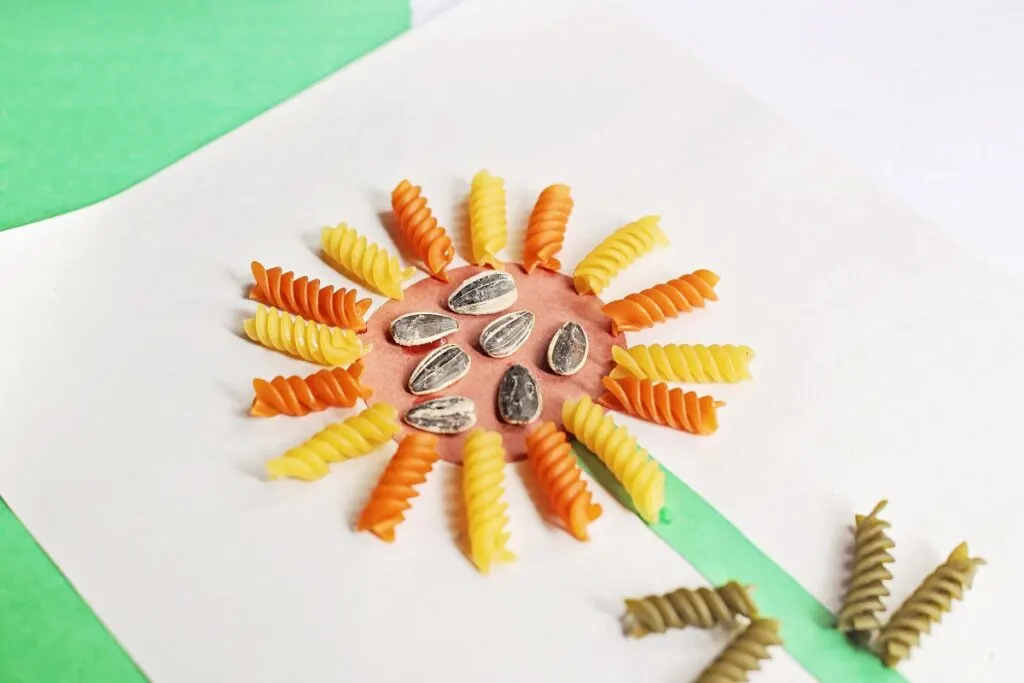 Close up of the top of the sunflower craft made with yellow and orange rotini pasta and sunflower seeds.