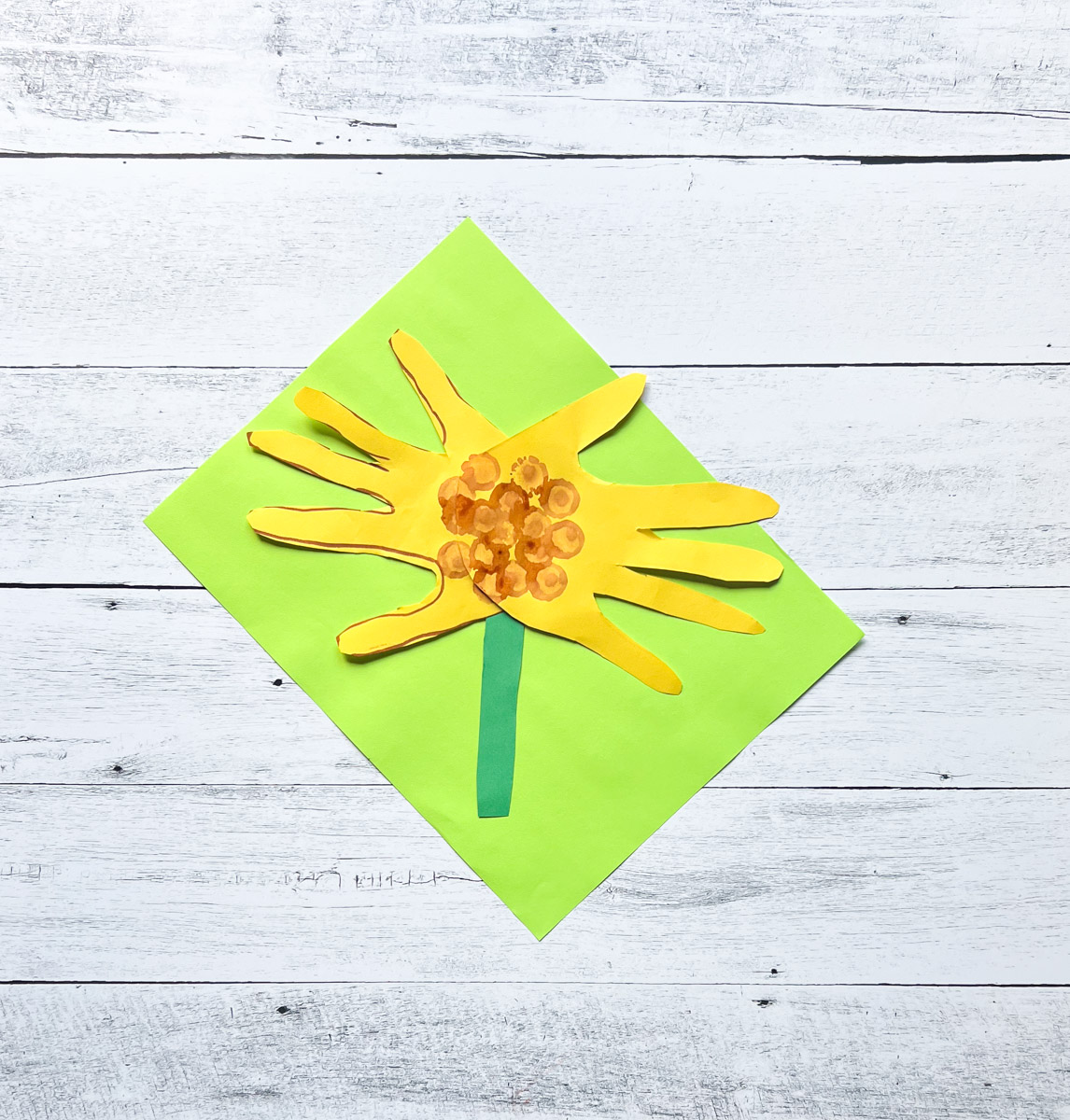 Finished handprint sunflower made out of construction paper laying on top of a bright green paper.