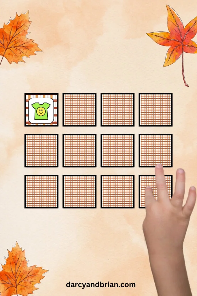 12 game cards laid out in a grid. 11 are face down and have a striped back. One card is flipped face up and has a t-shirt with a circle smiley face on it. A child's hand is selecting another card to flip over.