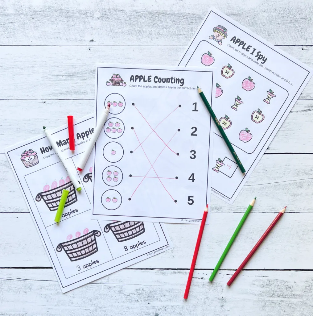 Three apple themed worksheets printed out and completed using red and green colored pencils. They are different counting exercises.