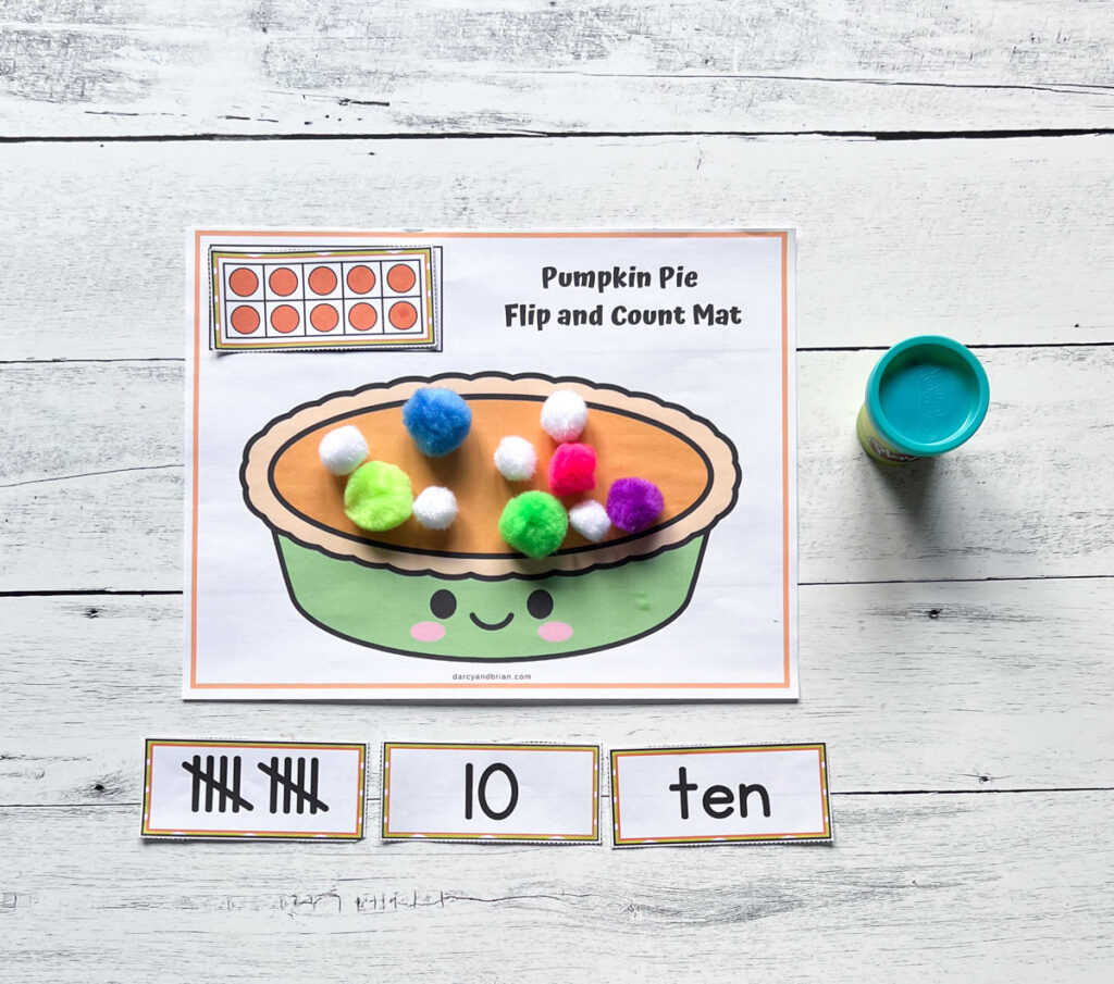 Different cards showing ten in different forms such as ten frame, tally marks, numeral, and word. Pie is covered in pom poms.