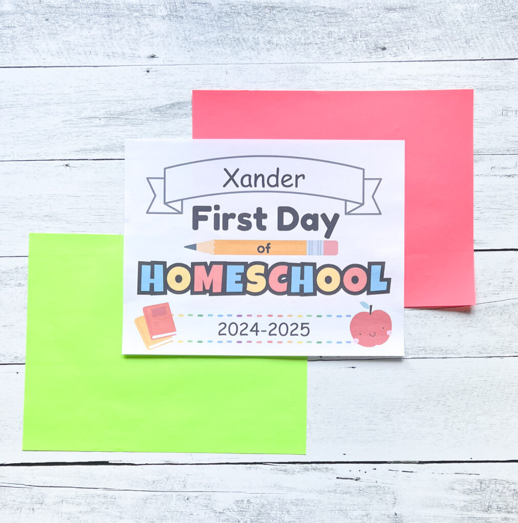 Printed out sign to hold up in back to school photos says Xander First Day of Homeschool 2024-2025. Name and year are editable. The page is laying on top of red and green cardstock.