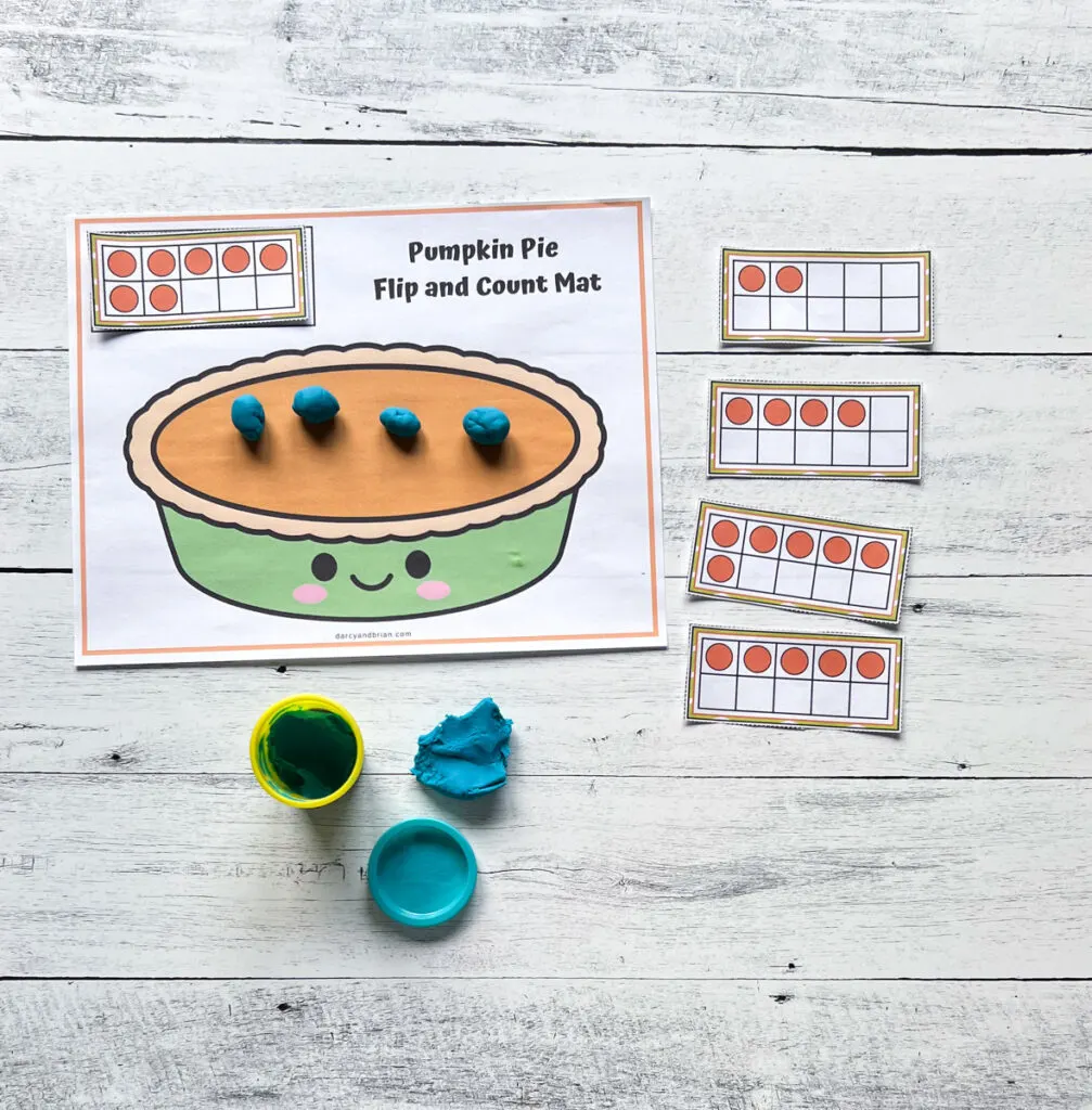 Cards with ten frames lined up next to pumpkin pie mat. Pieces of blue playdough rolled up and placed on top.