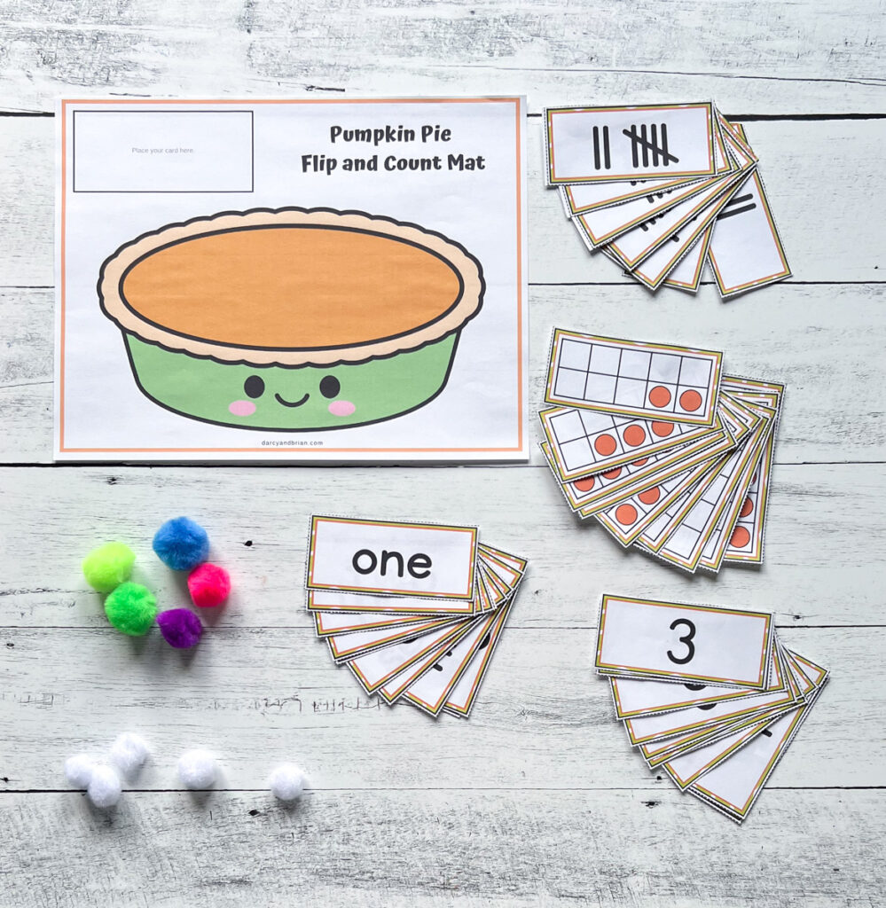 Pumpkin pie activity mat printed out. Number cards sorted in piles near mat along with pom poms.