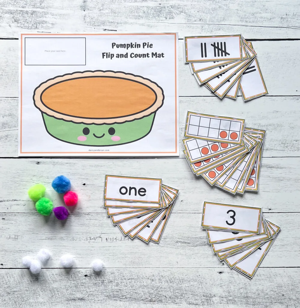 Pumpkin pie activity mat printed out. Number cards sorted in piles near mat along with pom poms.