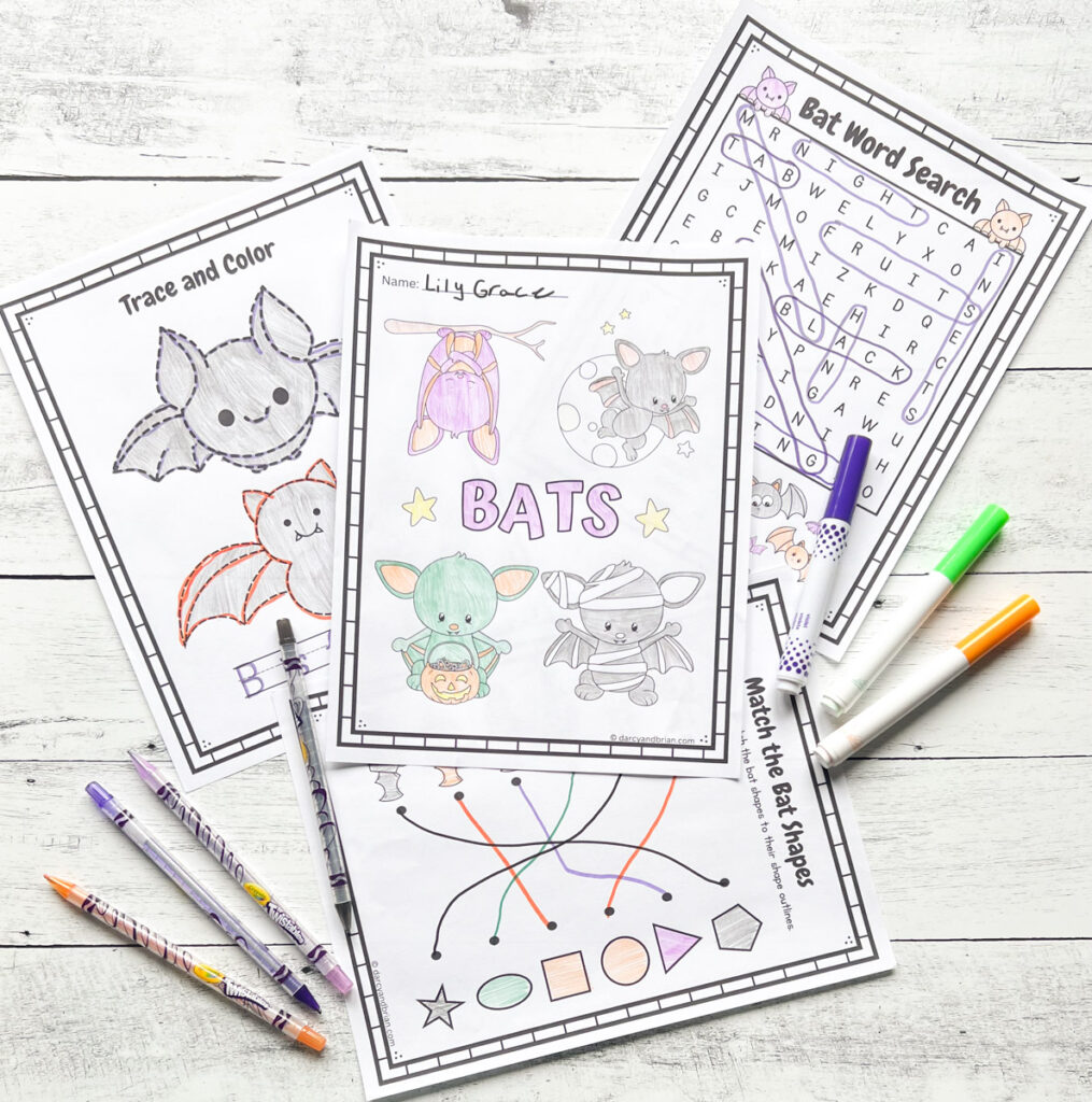 Four bat-themed worksheets placed in a black and white wood background with some color pens.