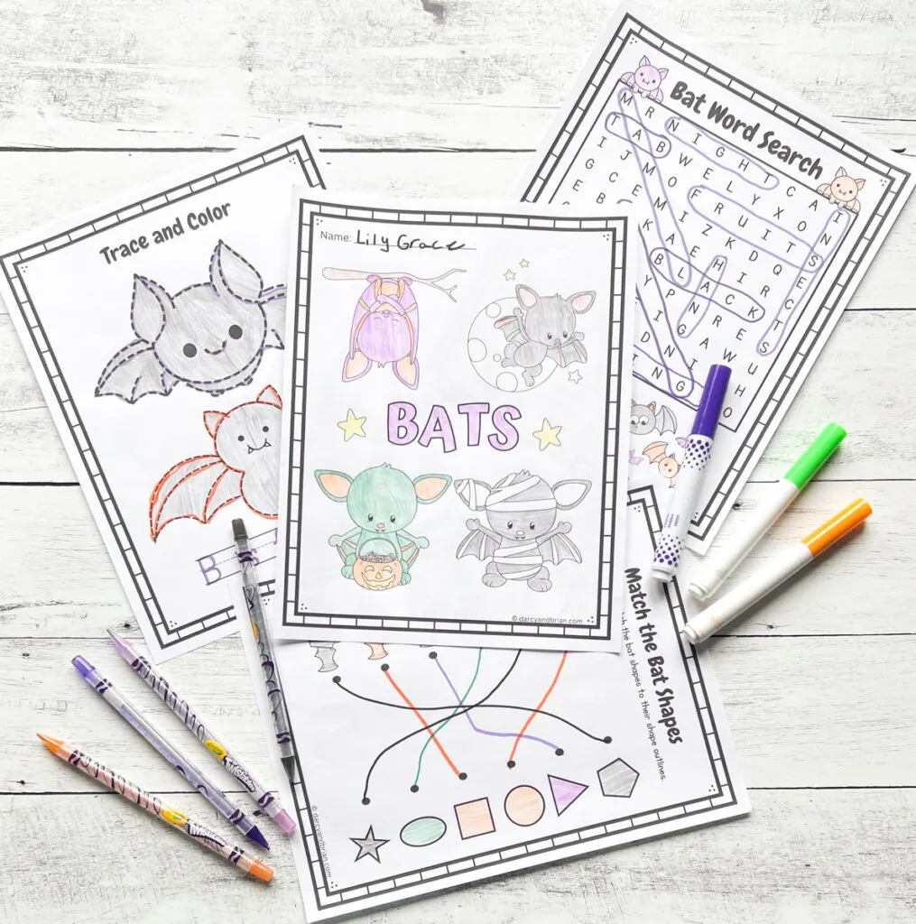 Four bat-themed worksheets placed in a black and white wood background with some color pens.