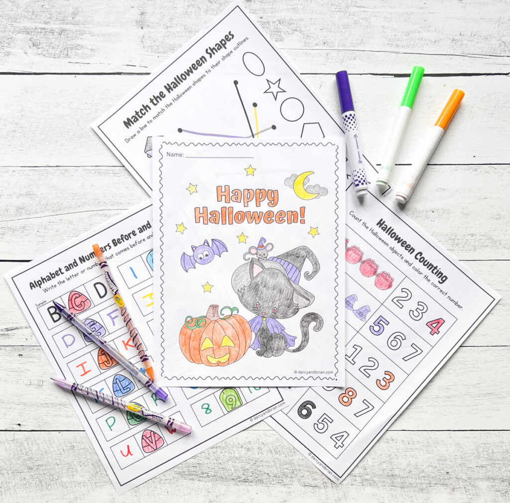 Four pages of the Halloween Worksheets for Kindergarten are placed in the black and white wood background along with some markers and color pencils.