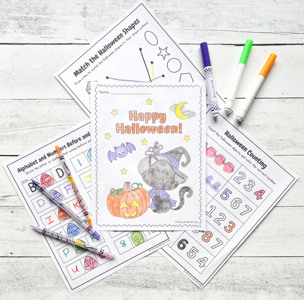 Four pages of the Halloween Worksheets for Kindergarten are placed in the black and white wood background along with some markers and color pencils.