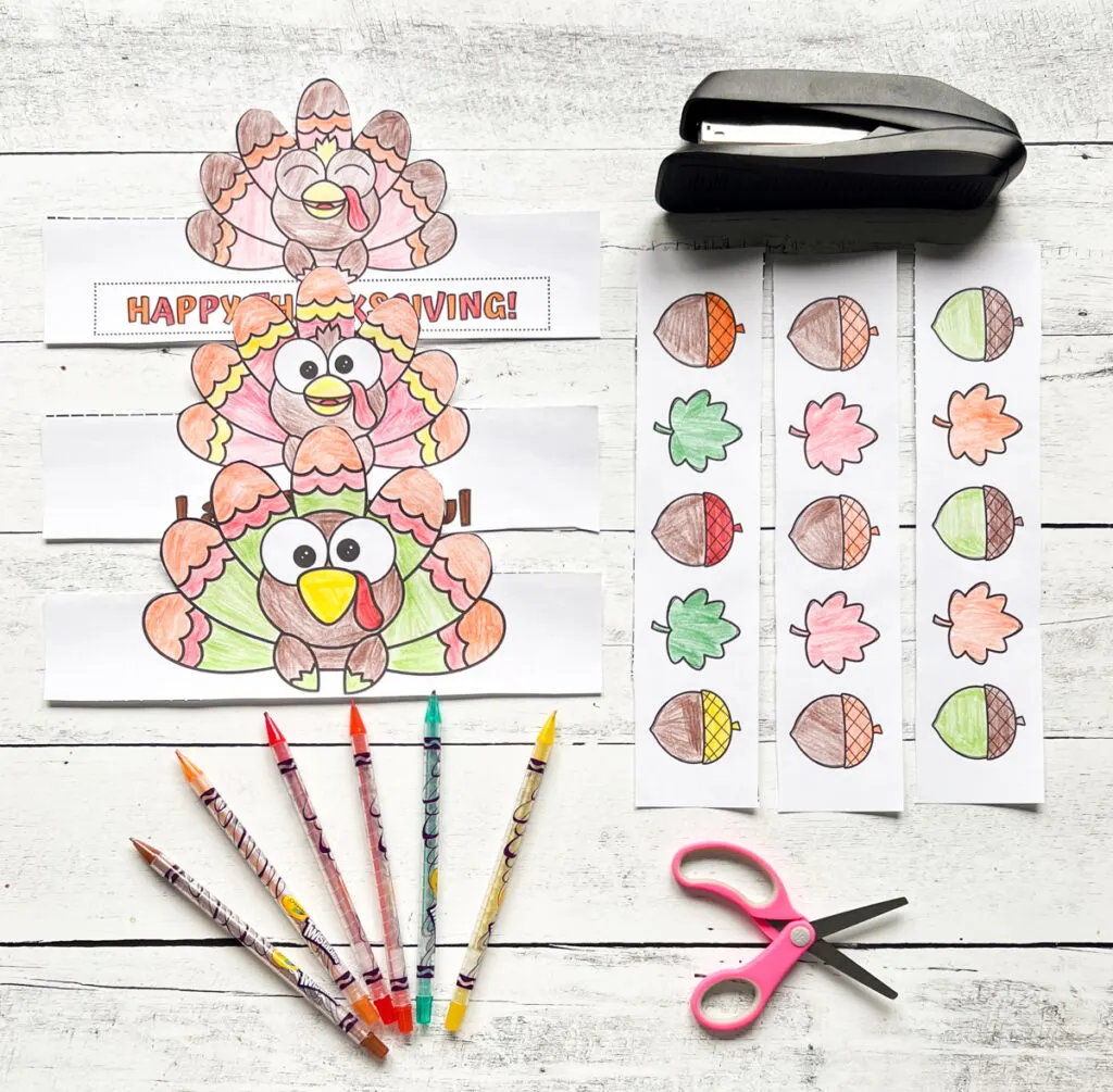 It has all the colored pages of Turkey Crown Craft with materials such as colored pen, scissors, stapler, all placed on a black and white wood background.