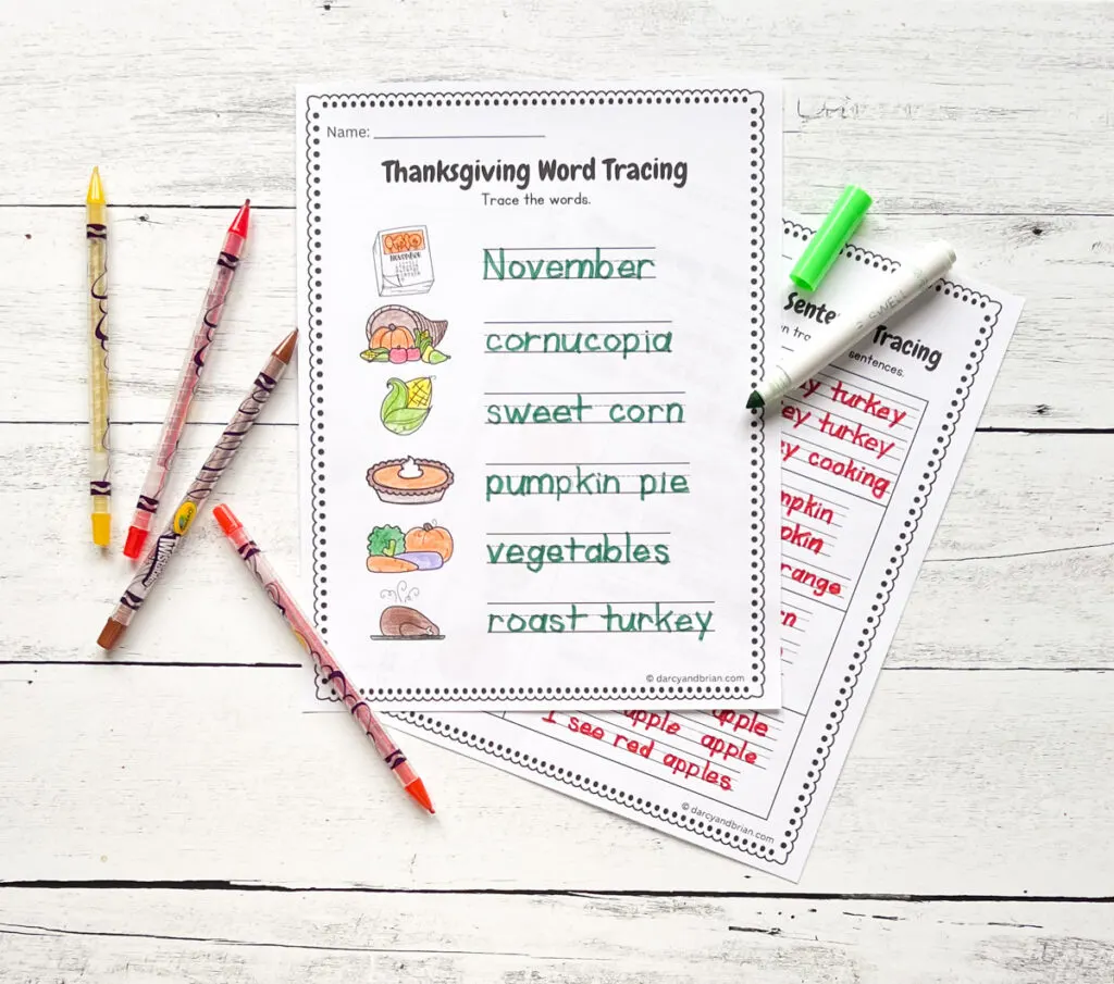 Two pages with words related to Thanksgiving dinner are traced using colorful pens or pencils placed in a black and white wood background.