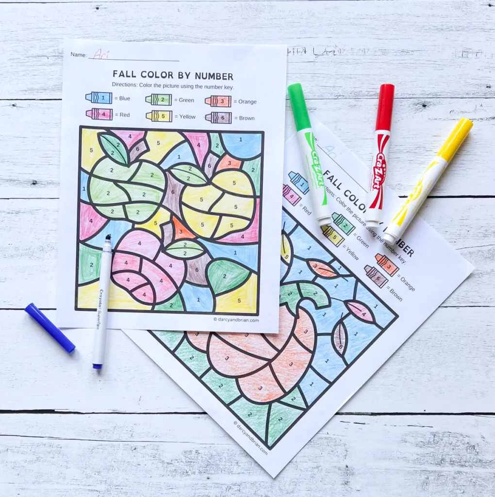 Two pictures featuring fall apples and a pumpkin are colored in. Markers lay next to the completed coloring sheets.