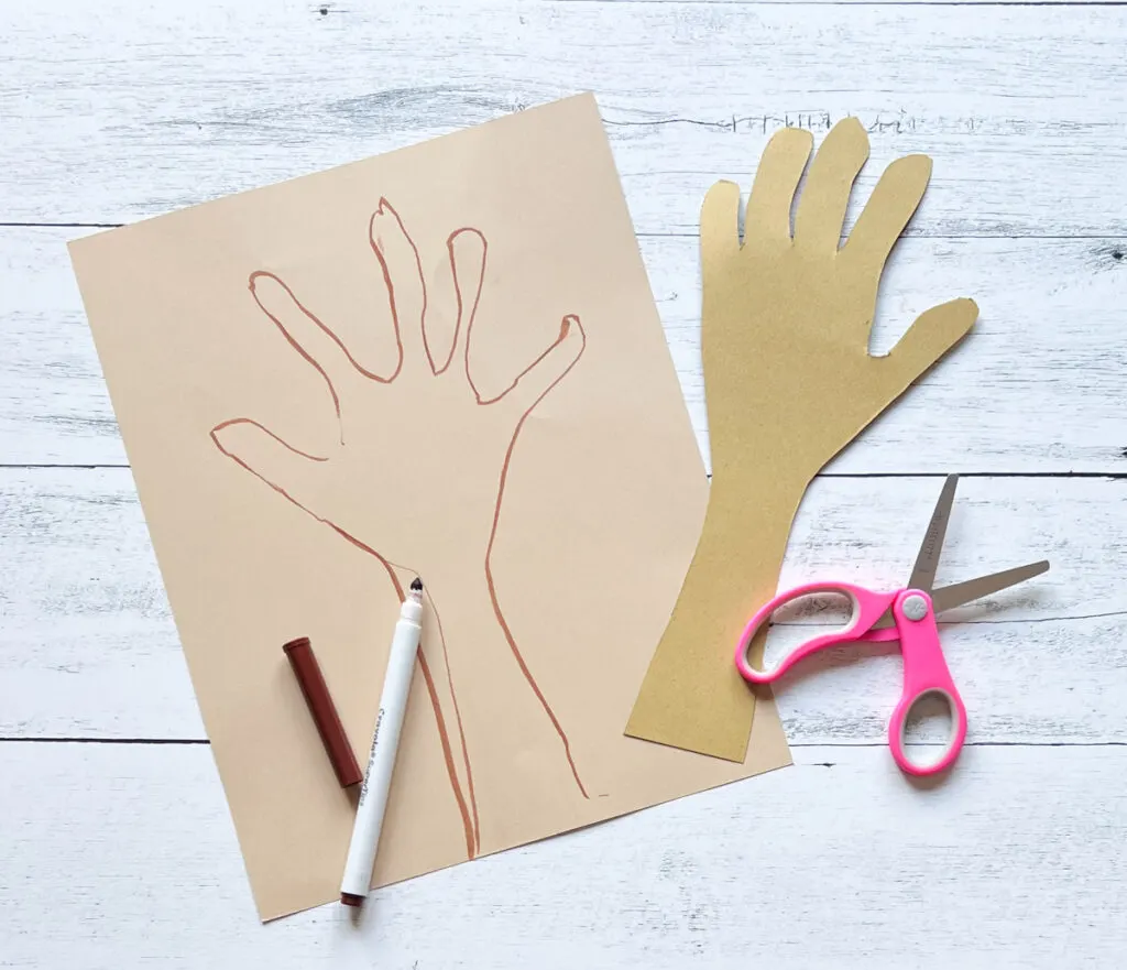 Outline of a hand traced with marker on light brown paper. A paper hand and part of the arm is cut out to be a tree trunk.