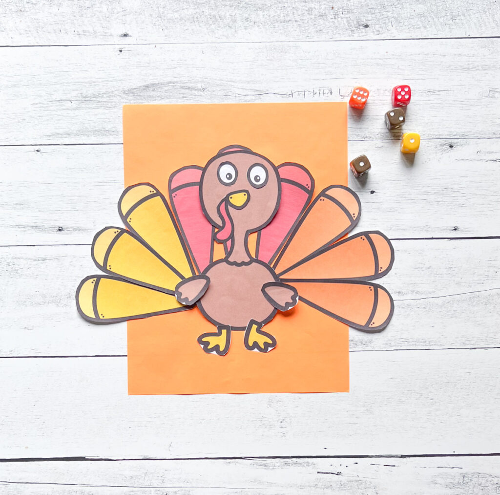 A page where the turkey creation has been made placed on an orange construction paper with some dice on the wood background.