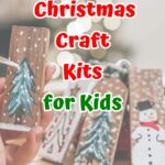 Red and green text outlined with white says Christmas Craft Kits for Kids over a background with small pieces of wood painted with snowmen and snowy pine trees.