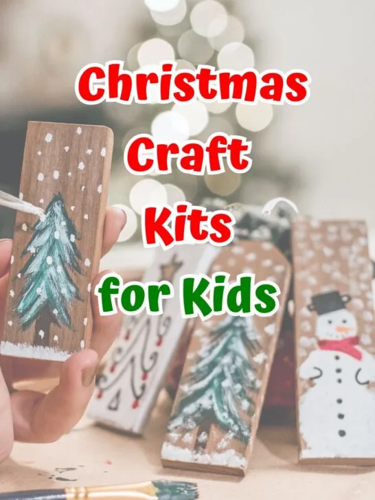 Red and green text outlined with white says Christmas Craft Kits for Kids over a background with small pieces of wood painted with snowmen and snowy pine trees.