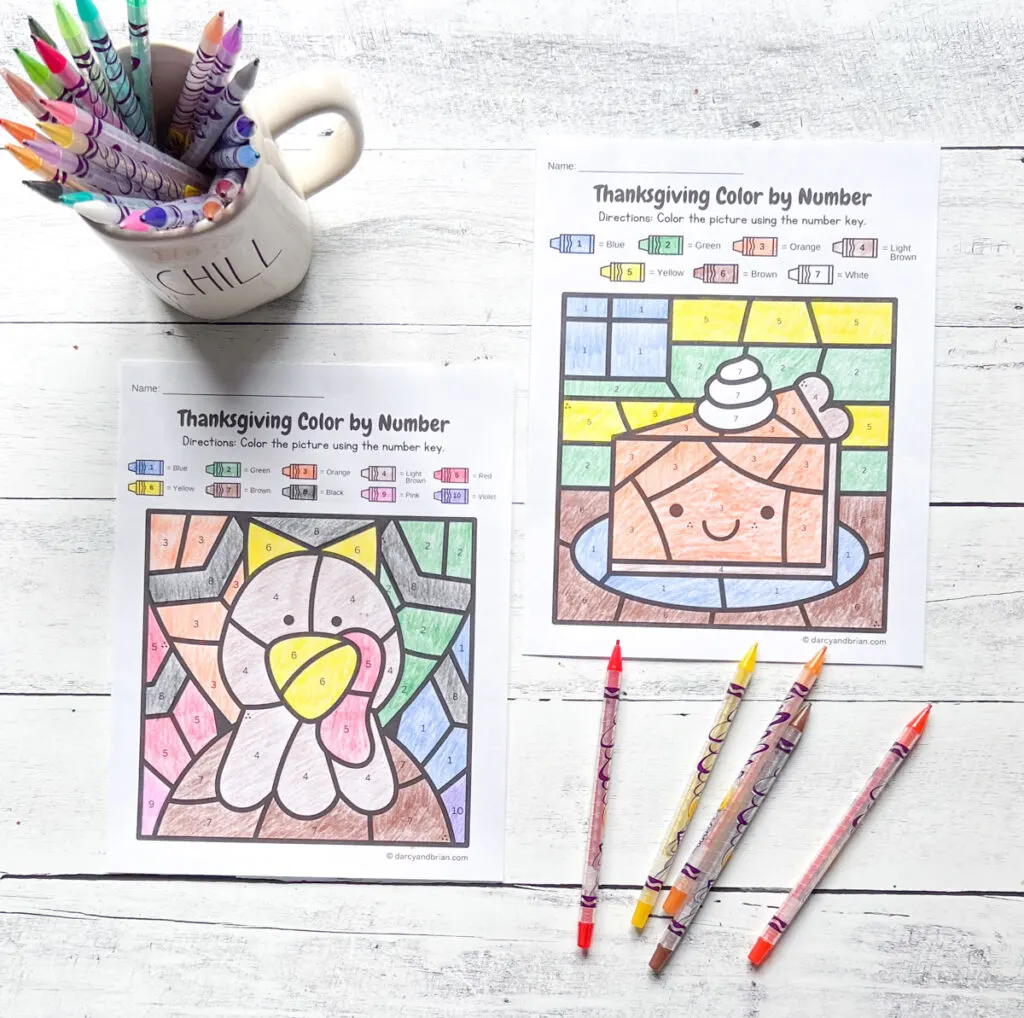 Completed turkey and pumpkin pie color by number pages. A mug full of twistable crayons sits next to the two pages.