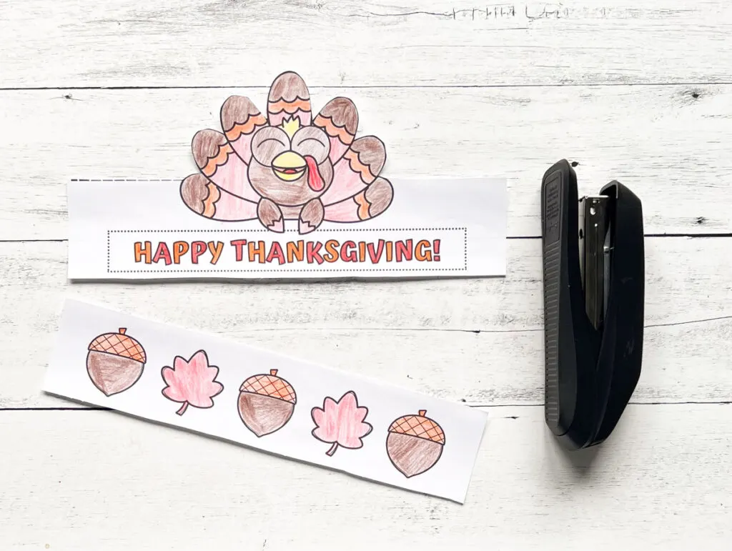 Thanksgiving turkey printable hat for kids is cut out and colored in. The front and the headband are laying on a white wood table next to a black stapler.