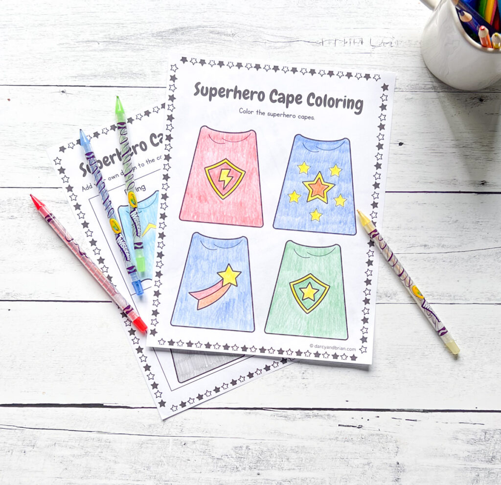 Coloring page of different superhero cape designs. Twistable crayons lay across the page.