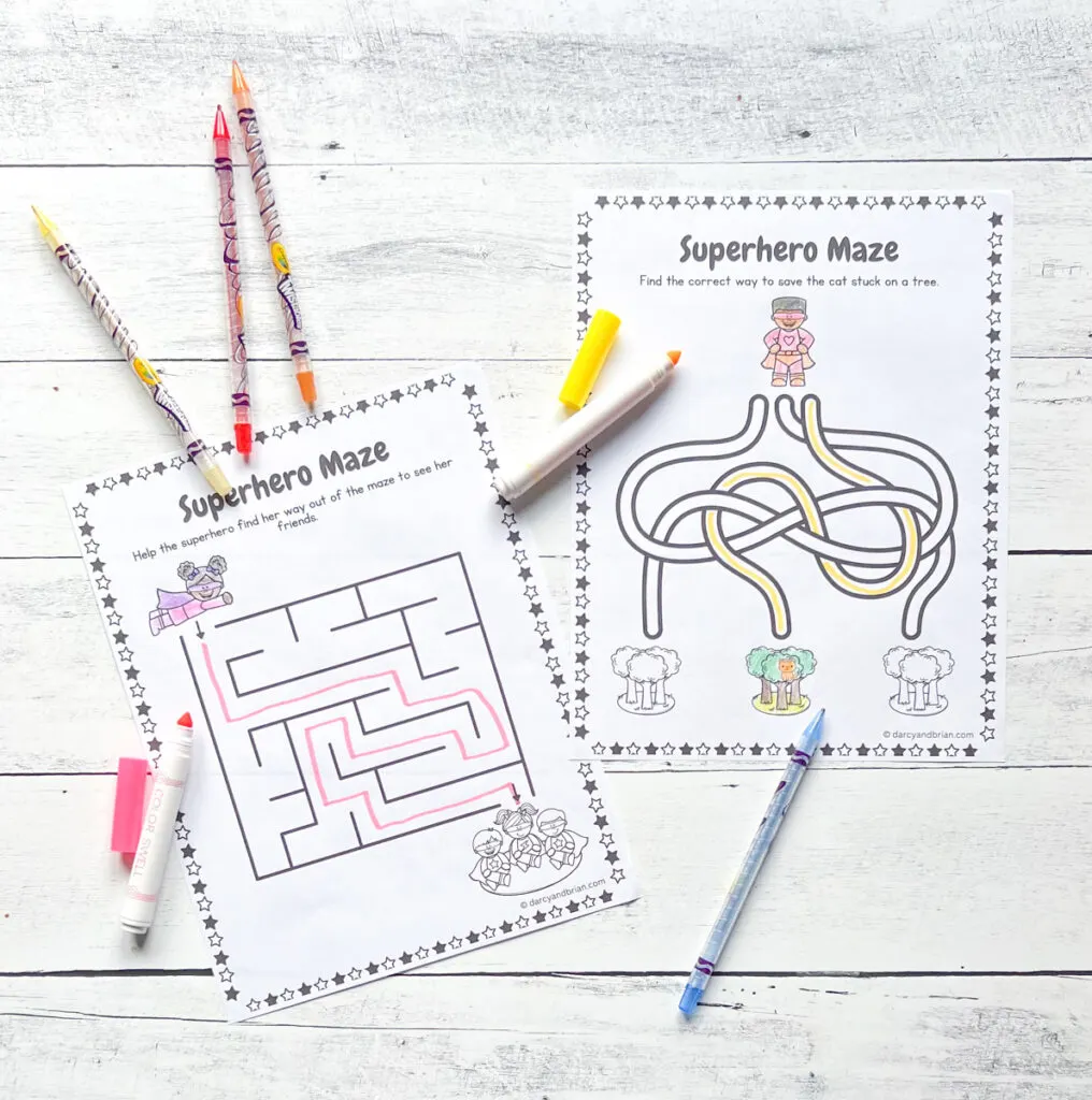 There are two Mazes activity pages with some markers and twistable crayons placed in a black and white wood background.