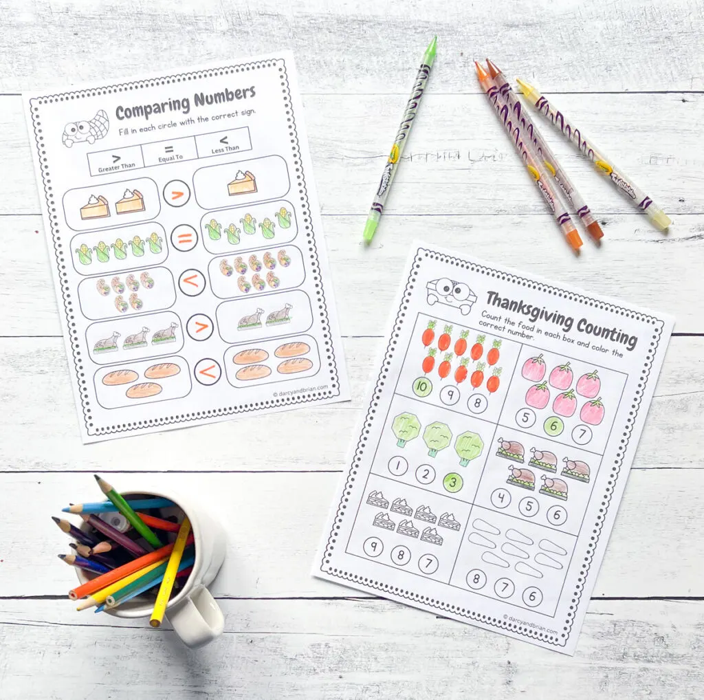 There are two completed worksheets laying on a white wood background. One features comparing numbers and the other counting. They all use different food items often found at Thanksgiving dinner.