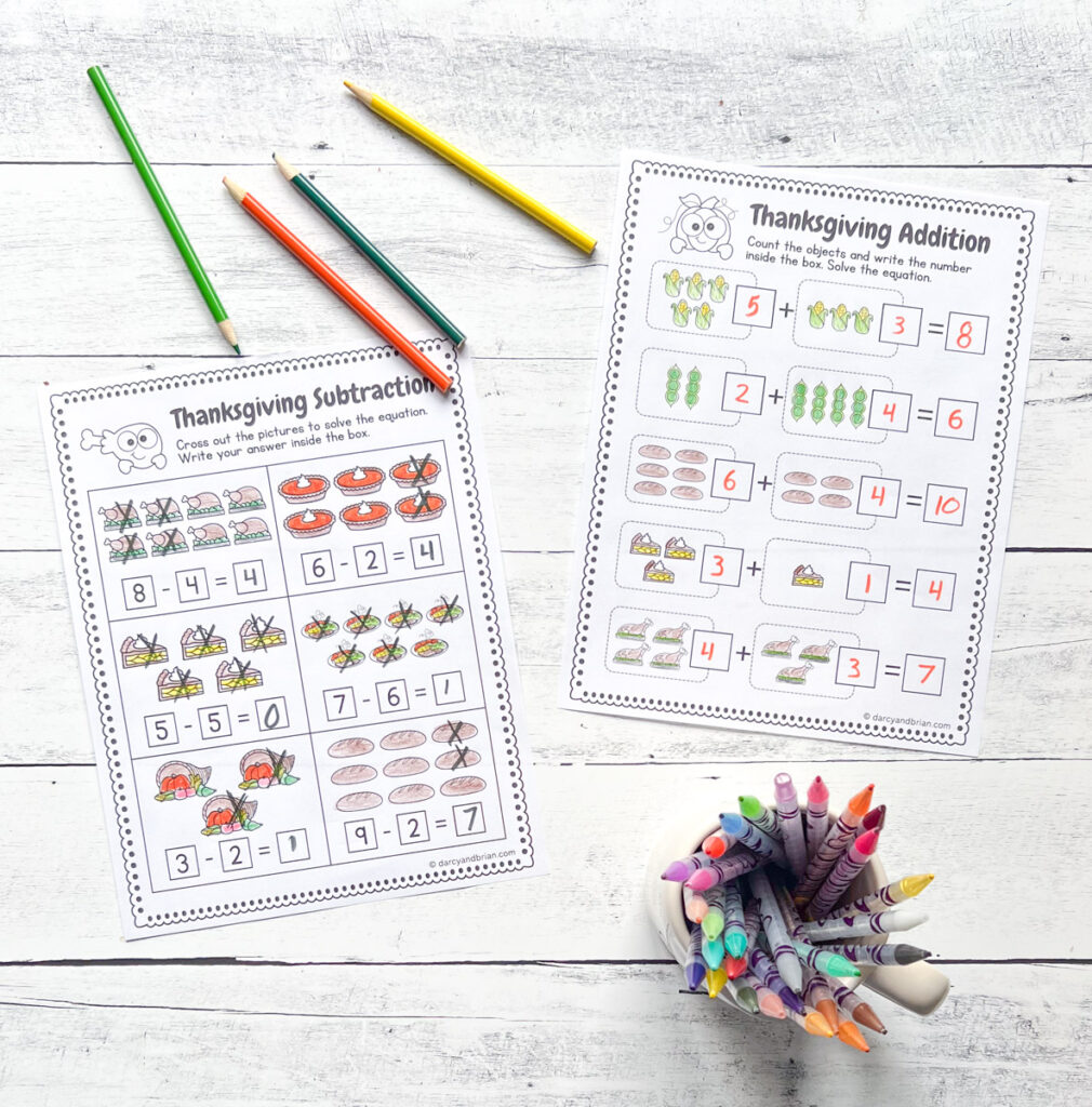 There are sample worksheets of Addition and Subtraction using Thanksgiving food items. There are some color pencils and color pens placed in a black and white wood background.