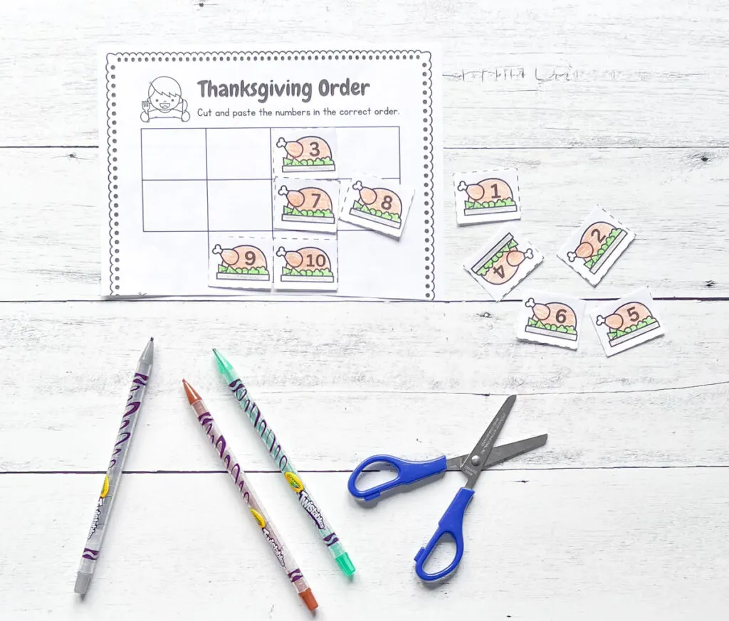 It has the printable worksheet Thanksgiving Order with some materials such as scissors and color pens placed in a black and white wood background.