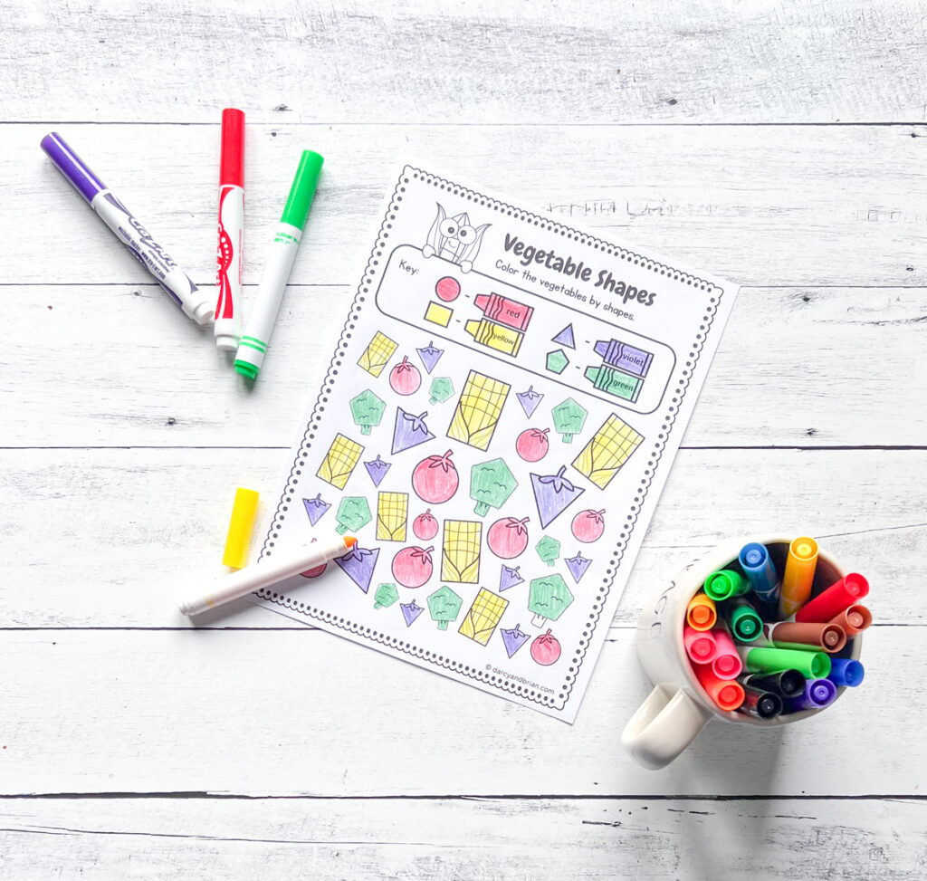 It has some markers with the Vegetable Shape worksheet placed in a black and white wood background.