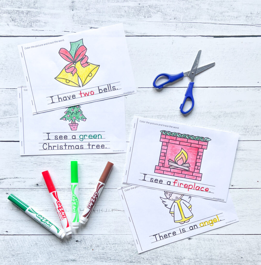 There are four printable book pages where kids can color and trace words for bells, trees, angel, and fireplace, along with scissors, marker, all placed in a black and white wood background.