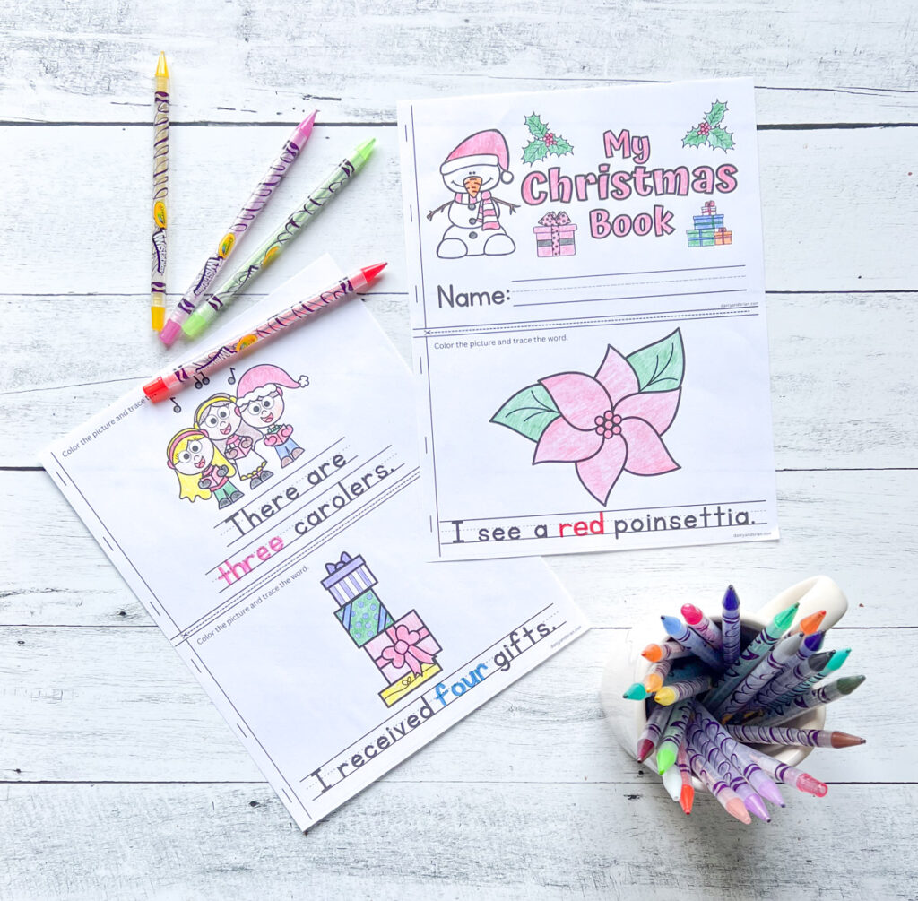 There are two pages of colored in mini Christmas worksheets with traced words, along with the materials like color pens, placed on a black and white wood background.