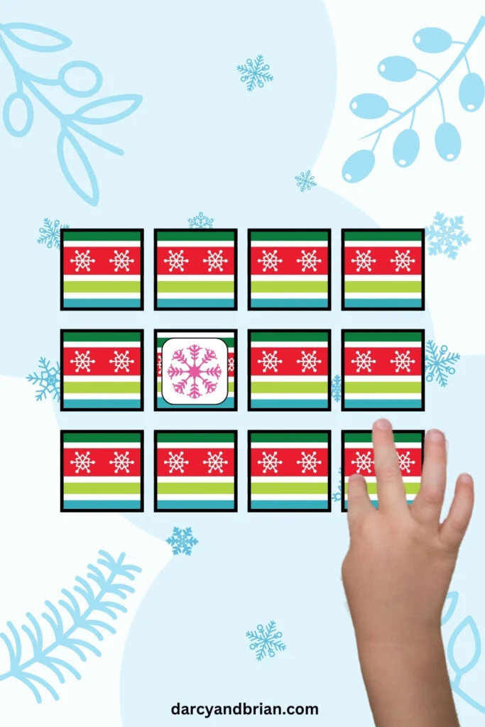 There are 12 cards shown with snowflake themed design placed in a snowy background. A young child's hand is pointing at one card.